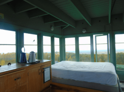 Cozy bedroom with a bed and large windows offering a scenic view of nature outside.