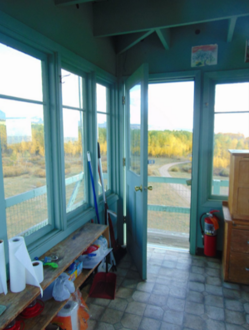 Interior of a lookout tower with green walls, open door, and a view of trees outside. Tools and supplies are on a bench.