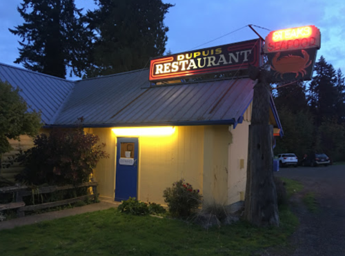 A cozy restaurant with a neon sign reading "Dupuis Restaurant," surrounded by trees and dim evening light.