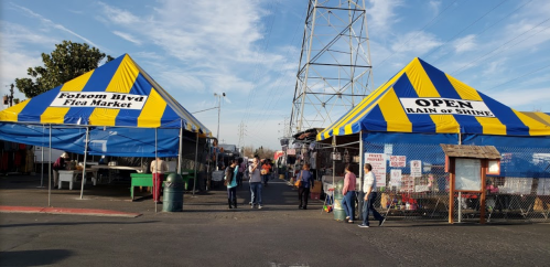 Colorful tents at Folsom Blvd Flea Market with people walking through, under a clear blue sky. Open rain or shine.