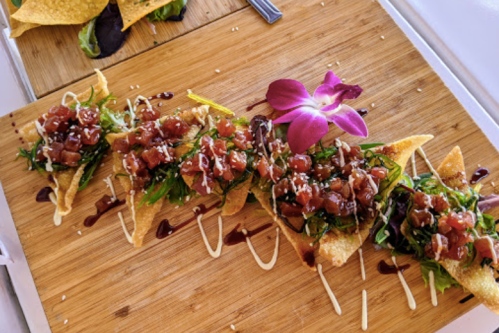 A wooden platter with crispy wontons topped with diced tuna, greens, sesame seeds, and a flower garnish.