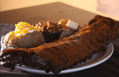 A plate featuring a large rack of ribs, baked potato with toppings, and a side of baked beans.