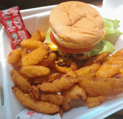 A cheeseburger with lettuce and tomato beside a serving of crispy fries and a packet of ketchup in a takeout container.