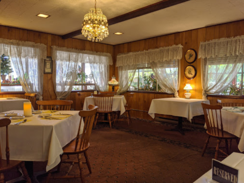 Cozy restaurant interior with wooden walls, white tablecloths, and a chandelier, featuring reserved tables and soft lighting.