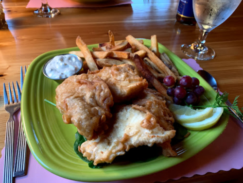 A vibrant plate of fried fish, fries, grapes, lemon, and tartar sauce on a wooden table.