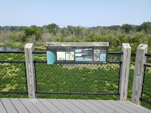 A viewing platform overlooking a lush green landscape with a sign about the Galien River and its wildlife.