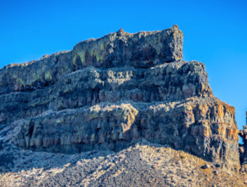 A rugged rock formation with layered cliffs under a clear blue sky.