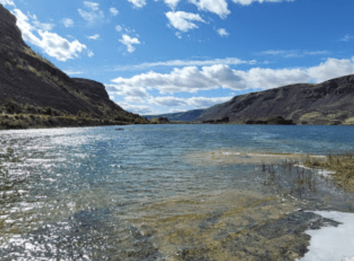 A serene river flows between rocky hills under a blue sky with scattered clouds.