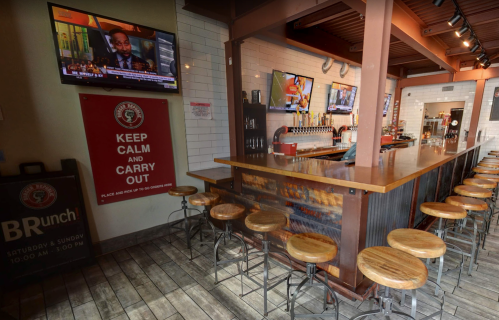 A modern bar area with wooden stools, multiple TVs, and a sign that says "Keep Calm and Carry Out."