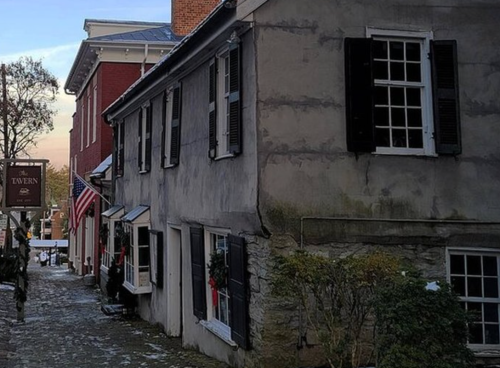 Historic buildings with shutters and festive decorations along a cobblestone street, featuring an American flag.