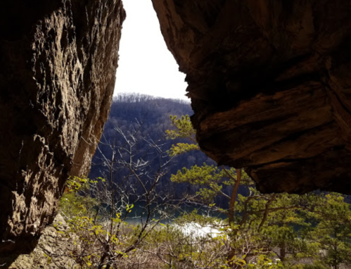 View through a rocky opening, revealing a serene landscape with trees and a river in the distance.