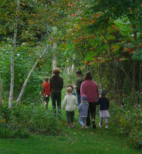 A group of adults and children walking along a lush, green path surrounded by trees and colorful foliage.