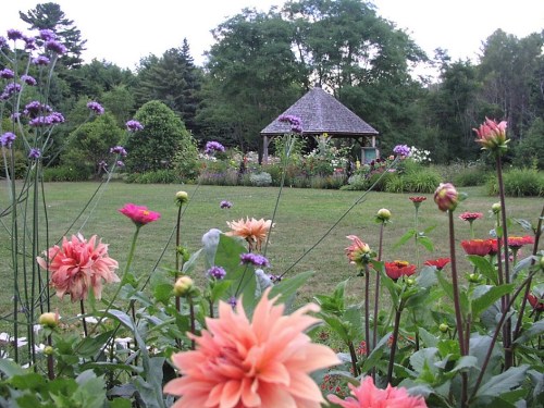 A vibrant garden filled with colorful flowers in the foreground, leading to a gazebo surrounded by lush greenery.