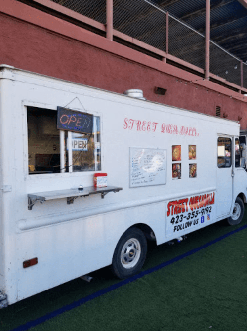 A food truck with a white exterior, featuring an "OPEN" sign and a menu displayed on the side.