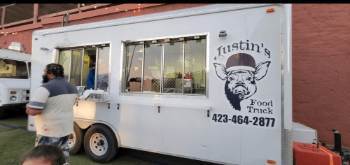 A food truck with a pig logo and the name "Justin's Food Truck" displayed, featuring a contact number.