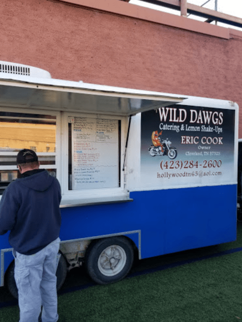 A food truck named "Wild Dawgs" with a menu displayed, featuring catering and lemon shake-ups. Owner: Eric Cook.