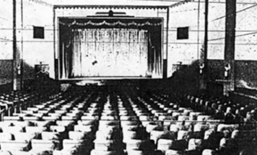 A vintage theater interior with rows of empty seats facing a stage draped with curtains.