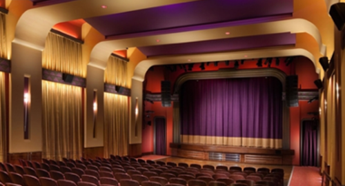 Interior of a theater featuring a purple curtain, rows of seats, and elegant lighting.