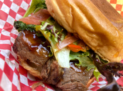 A close-up of a sandwich with grilled meat, lettuce, tomatoes, and sauce, served in a red and white checkered wrapper.