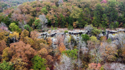 Aerial view of a rocky cliff surrounded by colorful autumn trees in a forested area.