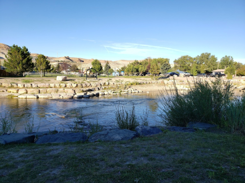 A serene river scene with trees and rocks, under a clear blue sky, showcasing a peaceful natural landscape.