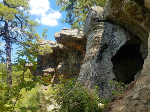 Rock formations surrounded by trees and greenery under a blue sky with scattered clouds.