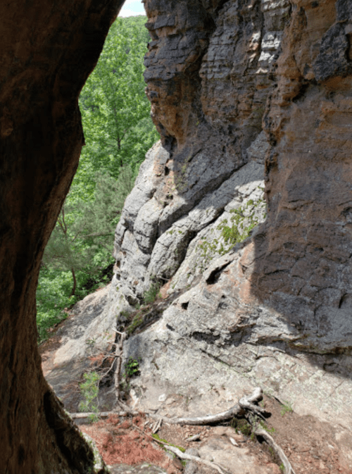 A rocky cliffside with greenery in the background, viewed through a natural arch or opening in the rock.
