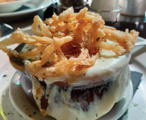 A bowl of creamy soup topped with crispy fried onions, garnished with herbs on a white plate.