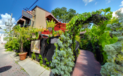 A charming restaurant entrance surrounded by lush greenery and vibrant plants on a sunny day.