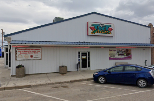 Exterior of TNT Casino with a blue roof, signage, and a parked car in front. Cloudy sky in the background.