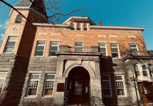 Historic brick building with stone accents, featuring large windows and a prominent archway entrance against a blue sky.