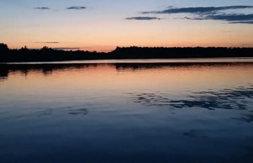 A serene lake at sunset, reflecting vibrant colors in the water with silhouettes of trees in the background.