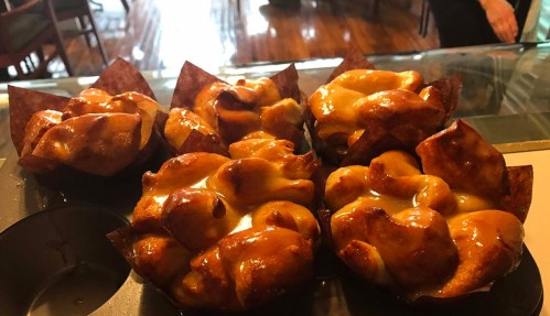 A close-up of golden-brown pastries in a muffin tin, with a glossy caramel glaze on top.