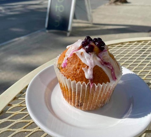A cupcake with a light frosting and blueberries on top, sitting on a white plate outdoors.
