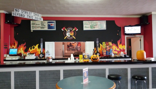 A concession stand with a fire-themed mural, snacks, drinks, and a Halloween pumpkin on display.