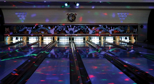 A brightly lit bowling alley with colorful lights reflecting on the lanes and pins, creating a festive atmosphere.