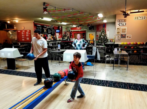 A bowling alley scene with a man and a child preparing to bowl, while a woman watches in the background.