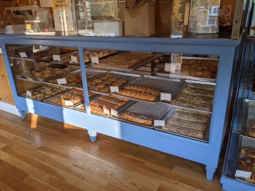 A display case filled with various baked goods, including pastries and bread, in a cozy bakery setting.
