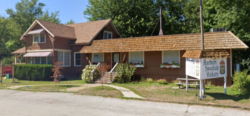 A charming bakery with a wooden exterior and a shingled roof, surrounded by greenery and a clear blue sky.