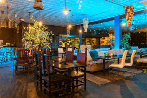 A stylish restaurant interior with wooden and upholstered seating, plants, and ambient lighting.
