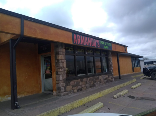 Exterior of Armando's Taco & Pasta Shop, featuring a colorful sign and stone accents, with cloudy skies above.