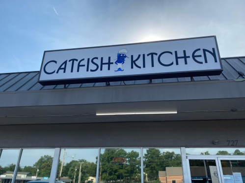 Sign for "Catfish Kitchen" with a cartoon chef, located at 727, under a clear blue sky.