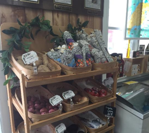 A wooden display with baskets of potatoes and colorful produce, labeled with prices, in a market setting.