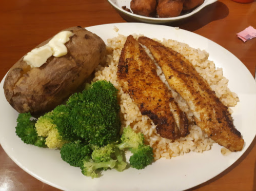 A plate with seasoned fish fillets, brown rice, steamed broccoli, and a baked potato with butter.