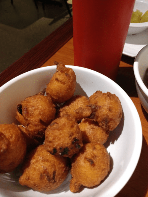 A bowl of golden-brown fried snacks, possibly fritters, next to a glass of red beverage.
