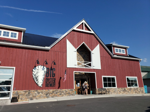 Exterior of Big Oyster Brewery, featuring a red barn-style building with stone accents and an American flag.