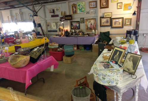 A vintage market scene with various antiques, colorful tables, and decorative items displayed in a spacious indoor area.