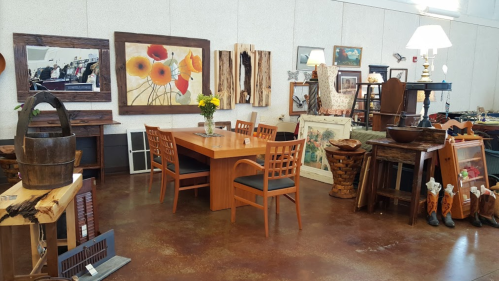A cozy furniture store featuring wooden tables, chairs, artwork, and decorative items in a warm, inviting space.