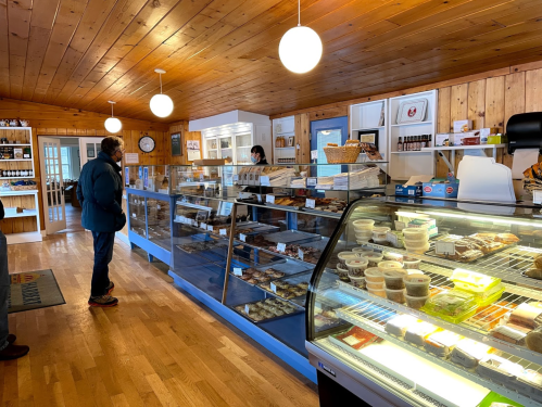 A cozy bakery interior with a customer at the counter, displaying various baked goods and treats in glass cases.