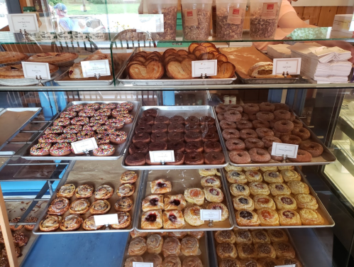 A display case filled with various pastries, including donuts, cinnamon rolls, and danishes, in a bakery setting.